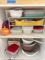 Cupboard shelf showing plastic containers, lids, onion keeper, colanders, utensil tray