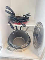 Stack of frying pans on upper shelf and nested pans with lid on lower shelf