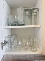 Cabinet shelves showing assortment of glass vases, tumblers, snifters and glasses