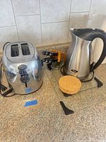 Full lot showing toaster, Oster kettle, knife block with knives, glass cutting board, cork trivets