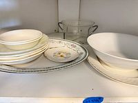Cabinet shelf with stacked bowls, platters, plate, large bowl and glass sugar bowl