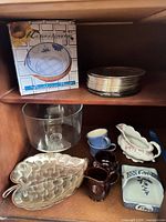 Cabinet shelf showing boxed bowl, stack of plates, vase, leaf dish, cups, gravy boat, small dish