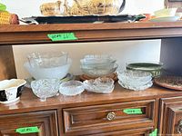 Shelf with assorted clear, frosted, green glass and ceramic bowls and dishes