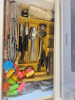 Drawer view showing whisks, knives, spoons, measuring spoons, corn holders, grater and strainer