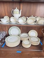 Full set on two cabinet shelves showing dinnerware stacks, cups, teapot, sugar, creamer