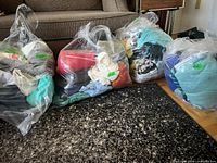Four clear plastic bags filled with assorted women’s garments placed on floor