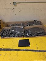 Four open cartons containing stacks of individually bagged black mouse pads; one mouse pad displayed in front