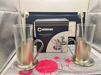Full set showing two glasses in holders with saucers and spoons, box in background