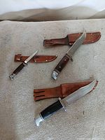 Three fixed-blade knives with sheaths on table