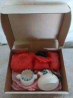 Open box showing ceramic snowman pieces wrapped in red tissue