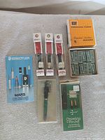 All items laid out: catalog, three Rapidograph pens in boxes, Pelikan pen in case, Osmiroid set, Eberhard Faber eraser box and contents