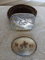 Both buckles side by side; champion buckle shown attached to rolled leather belt
