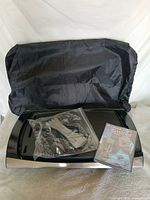 Overall lot showing grill/griddle base, storage cover, bagged accessories and sealed DVD