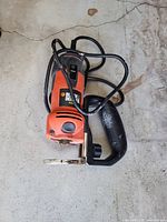 Top view of Black & Decker orange/black trim router with cord and handle visible on concrete floor