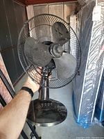 Front view of black pedestal fan showing blades, grill, base, and cord