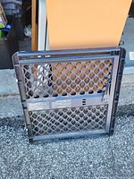 Front view of black plastic hardware-mounted baby gate showing lattice design and latch