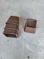 Five brown plastic square leg caps, four stacked together and one separate