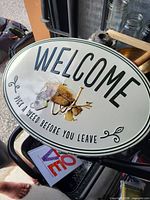 Front view of oval metal welcome sign showing text, illustration and border