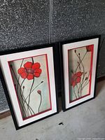 Two framed vertical floral prints with black frames leaning against wall