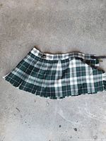 Full view of green/white/black tartan pleated kilt skirt showing pattern, pleats, buckle straps and hem condition
