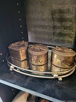 Three brass tins with mirror serving tray on shelf