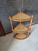 Overall view of the three-tier triangular wood corner shelf showing cane rattan panels and spindle supports