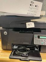 Printer front view with output tray open, HP logo visible, USB cable placed in tray, toner box on top