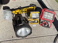 Group view of four floodlights and collapsed yellow tripod stand on concrete surface