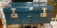 Front view of metal trunk showing color, latches, recessed handle, overall wear