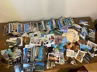 Wide view of all postcards spread on table including folded accordions and loose stacks
