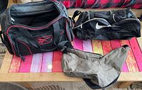 Three bags on table: Reebok duffel, Nike duffel, brown sling