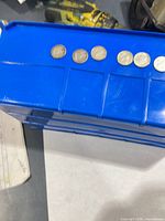 Six coins aligned on blue plastic surface, showing reverse designs