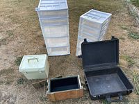 Two plastic drawer towers, green cooler box, wood crate, black protective case laid out on grass