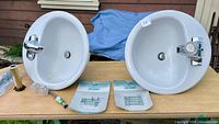 Both sinks, faucets, drains, supply lines, bolt kits and drain pipe displayed on table
