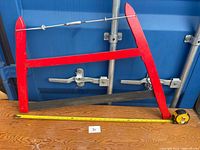 Full view of bow saw against blue background with tape measure showing length