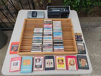 Overview of lot: rack filled with cassette tapes, two portable players on top edge, eight 8-track cartridges lined in front