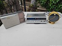 Overall view of three items: Magnavox portable radio, GE clock radio, Howard Miller desk clock