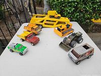 Overview of seven vintage Tonka and Buddy L toy vehicles and car-carrier trailer on table
