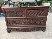 Front view showing three drawers with carved floral and lattice designs and metal drop handles