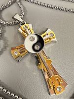 close-up of two-tone stainless steel cross pendant with yin yang symbol and rhinestones