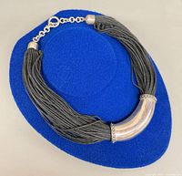 Front view of necklace on blue display showing silver curve and black strands