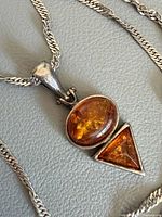 Close-up of silver pendant with oval and triangular amber stones on chain