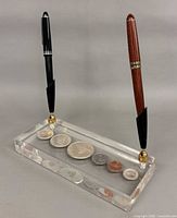 Overall view of lucite pen holder with two pens and visible coins