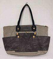 Front view of tote bag showing two-tone leather, front pockets, handles, hardware