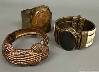Three bracelets: crocodile bangle, brass cuff with brown stone, hinged segmented cuff with black stone