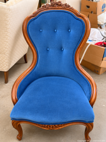 Front view of chair showing blue velvet upholstery, tufted back, carved wood frame