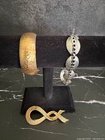 Group shot showing gold cuff bracelet, silver link bracelet and gold ribbon brooch on display stand