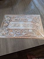 Front view of embossed "PSYCH WARD" sign showing design, color, text