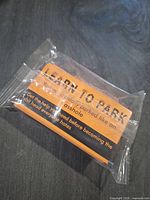Shrink-wrapped pack of orange and black parking warning cards on dark surface