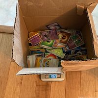 Open box of loose Pokémon cards on scale reading 4.982 lbs